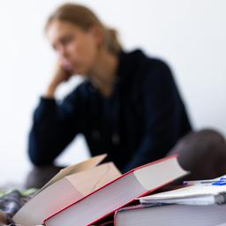 Eine Studentin sitzt auf dem Bett in ihrem Zimmer. Vor ihr liegen Lehrbücher und ein Notizbuch.