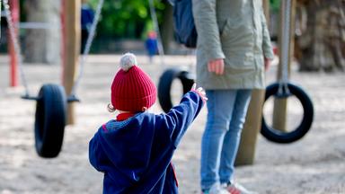 Ein Kind steht mit seiner Mutter auf einem Spielplatz.