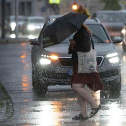Eine Passantin überquert bei starkem Regen eine Straße in Bautzen, Sachsen, mit einem Regenschirm