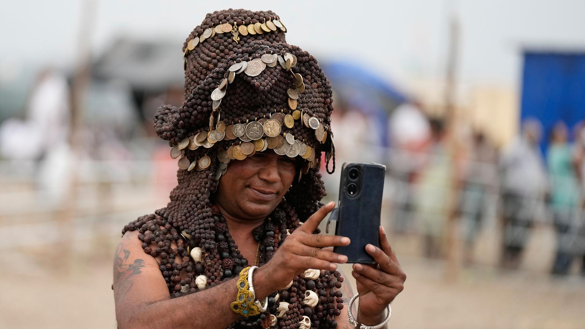 Ein Mann in traditioneller Kleidung nimmt ein Handyvideo auf. | Channi Anand/AP/dpa
