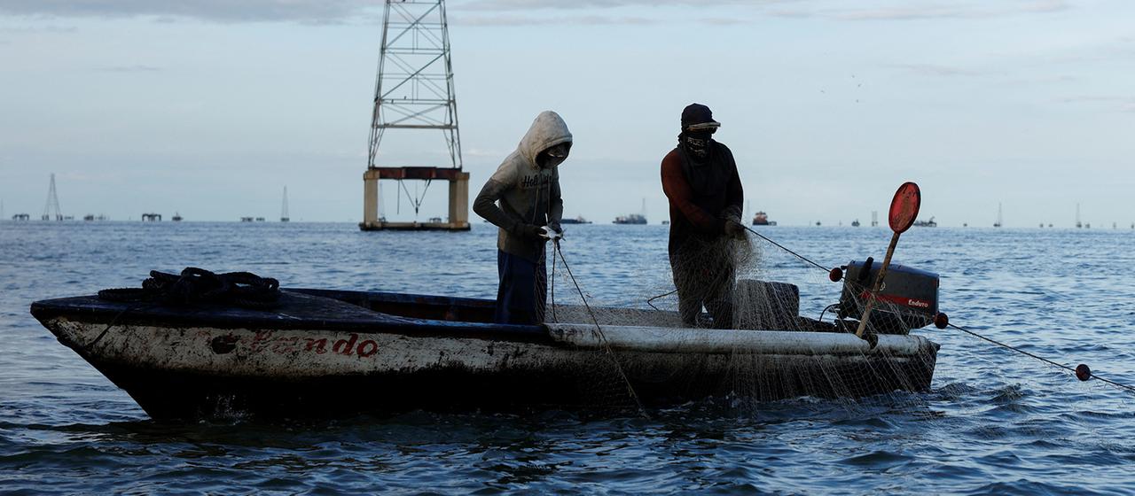 Fischer ziehen ihre Netze in der Nähe eines verlassenen Ölförderturms am Ufer des Maracaibo-Sees an Bord.