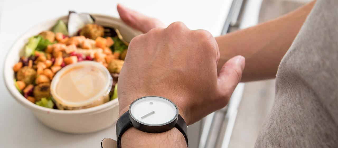 Ein Mann schaut auf seine Armbanduhr, während er nach einem Salat greift.