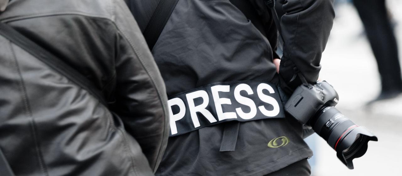 Ein Fotoreporter trägt  einen Aufnäher mit dem Text "Press""auf seiner Jacke.