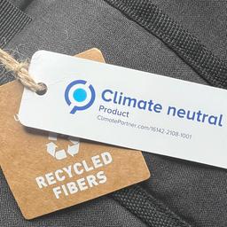 An einem Rucksack hängen zwei Anhänger, die darauf hinweisen, dass er ein klimaneutrales Produkt ist und aus recycelten Fasern besteht. 