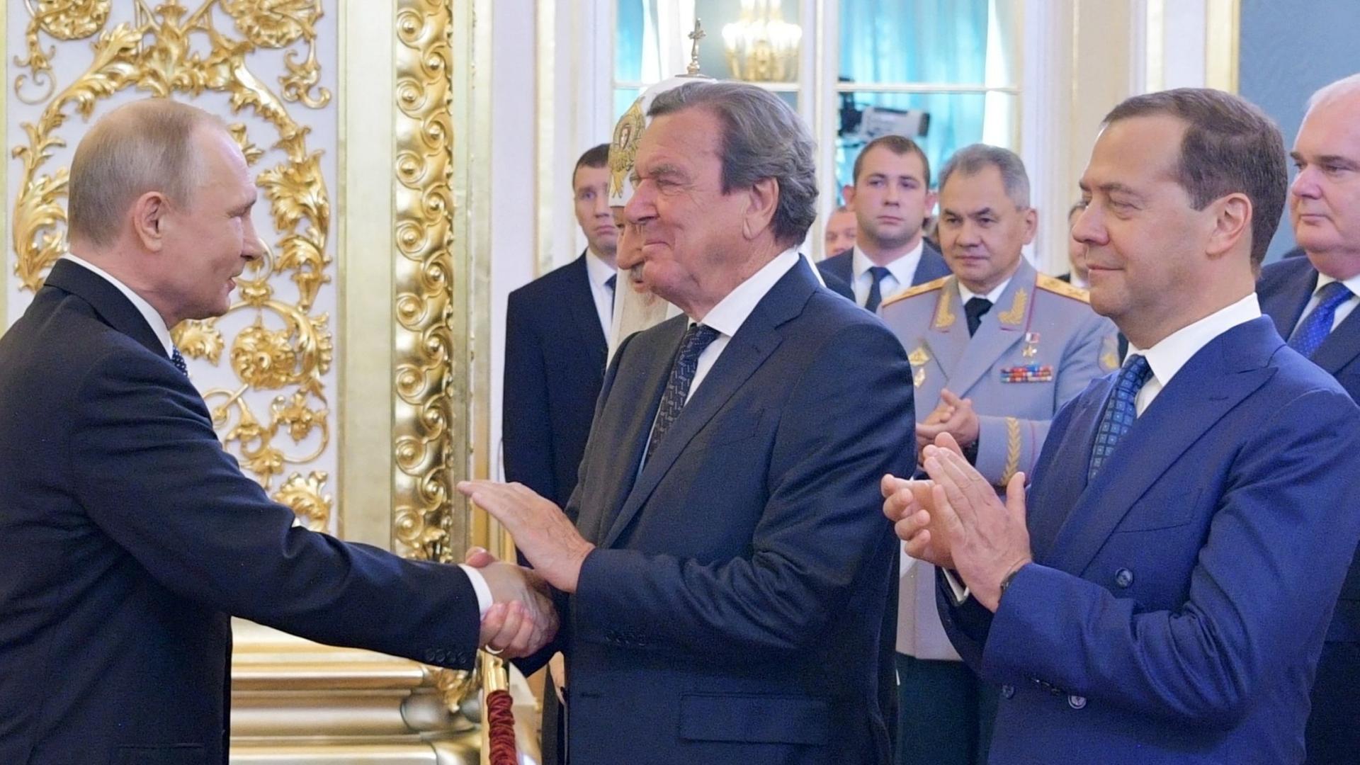 Putin schüttelt Schröder im Moskauer Kreml (Russland) die Hand, während Medwedew applaudiert. | AFP