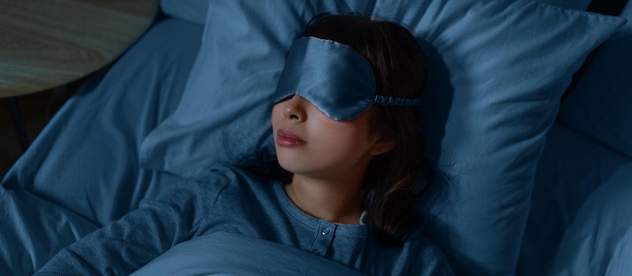 Eine Frau schläft nachts zu Hause im Bett mit Schlafmaske.