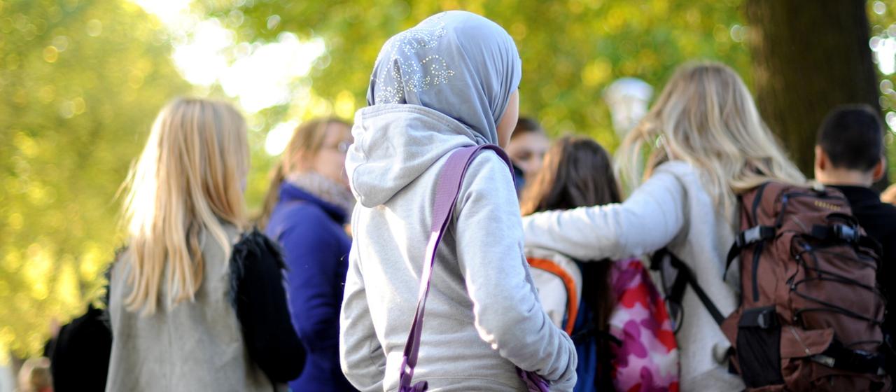 Ein junges Mädchen trägt ein Kopftuch auf dem Schulhof.