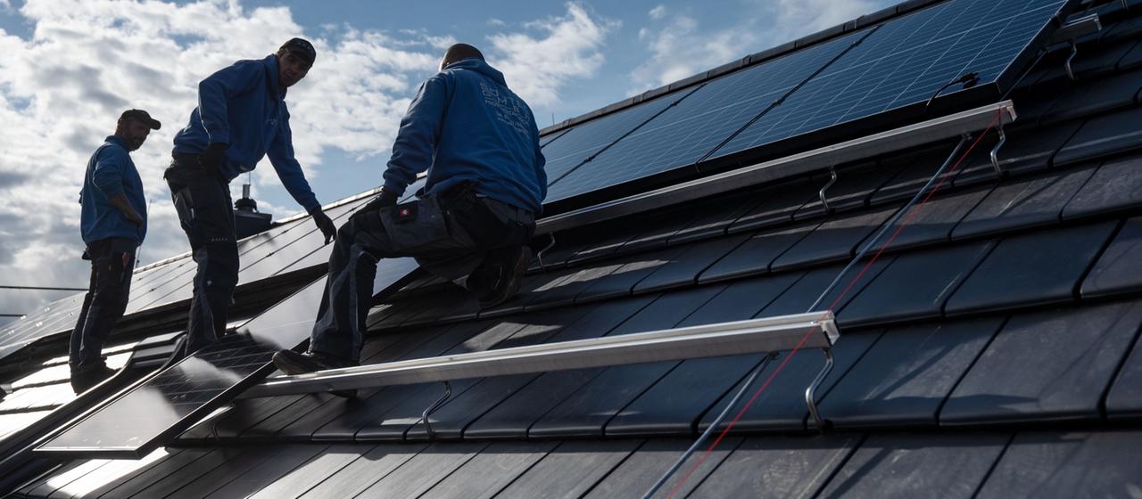 Mitarbeiter einer Firma montieren Photovoltaikmodule auf dem Dach eines Wohnhauses.