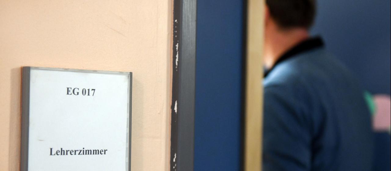 Ein Mann geht an einem Schild vorbei, das den Weg zum Lehrerzimmer weist.