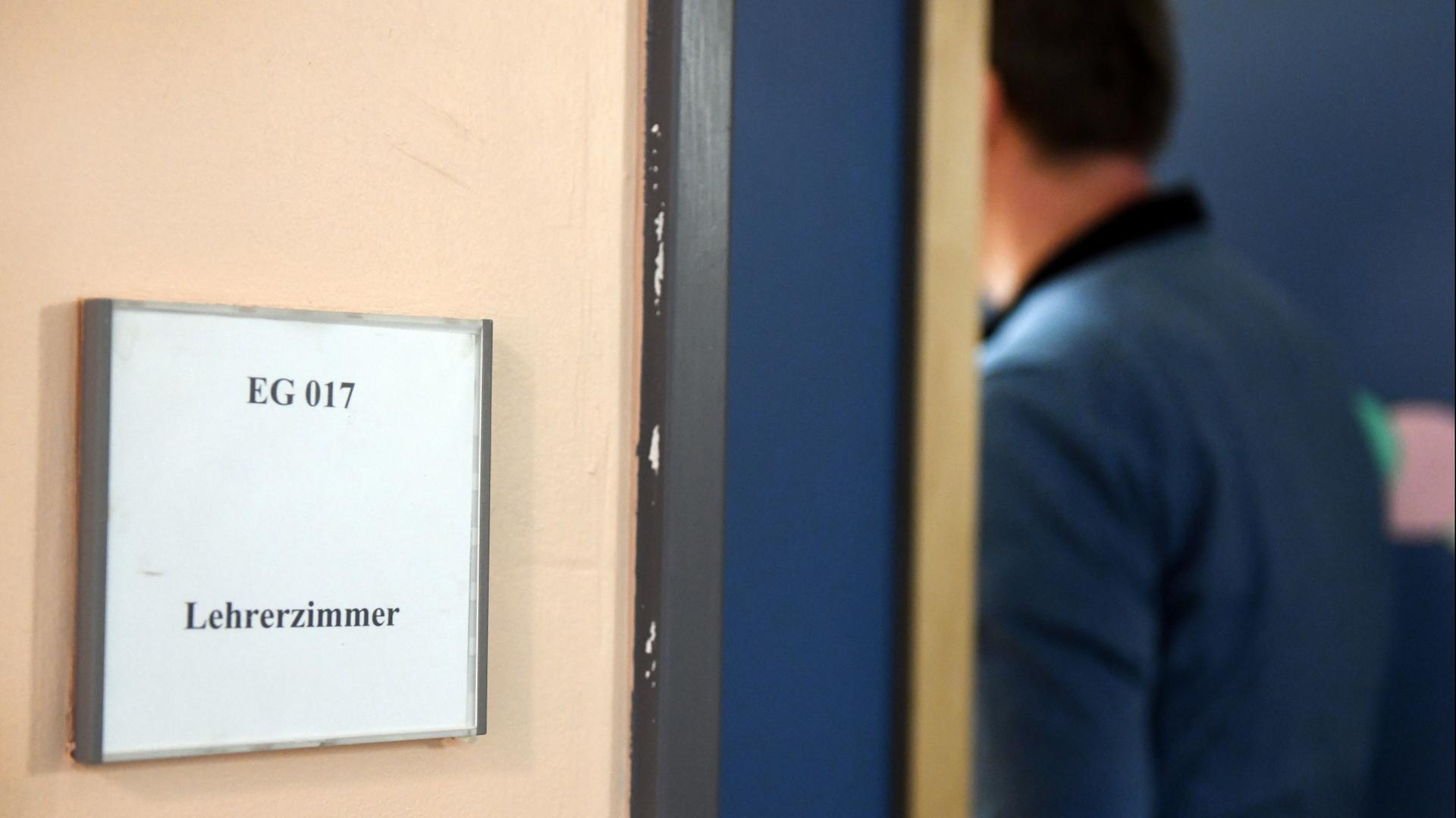 Ein Mann geht an einem Schild vorbei, das den Weg zum Lehrerzimmer weist. | Maurizio Gambarini/dpa