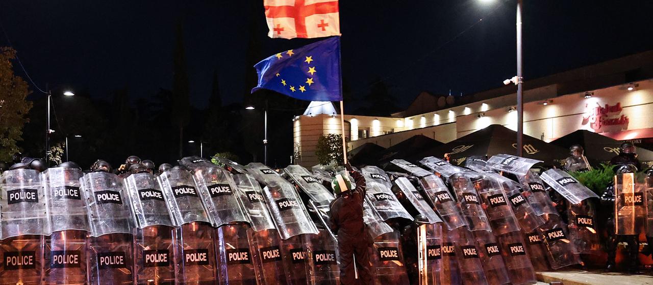 Ein Demonstrant schwenkt vor der Bereitschaftspolizei in der Innenstadt von Tiflis eine georgische und eine EU-Flagge. (Archivbild: 4. Oktober 2025) | AFP Ein Demonstrant schwenkt vor der Bereitschaftspolizei in der Innenstadt von Tiflis eine georgische und eine EU-Flagge. (Archivbild: 4. Oktober 2025)