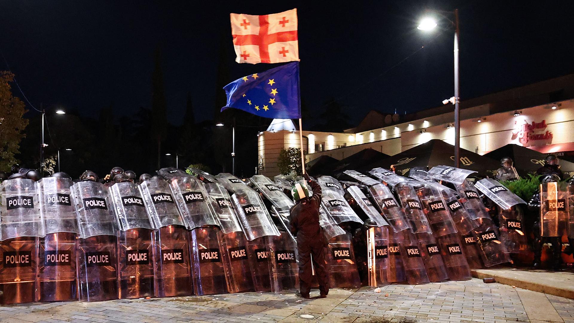 Ein Demonstrant schwenkt in der Innenstadt von Tiflis vor der Bereitschaftspolizei eine georgische und eine EU-Flagge. (Archivbild: 4.10.2025) | AFP