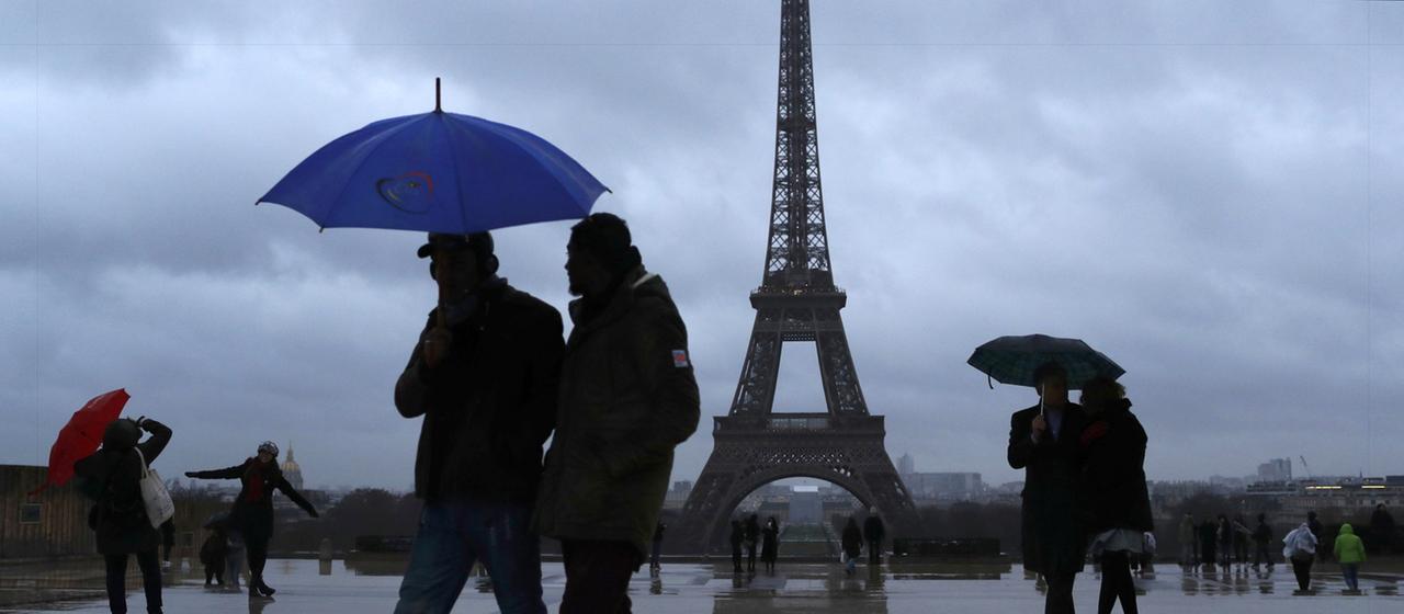 Passanten ducken sich vor dem Eiffelturm in Paris unter ihren Regenschirm.