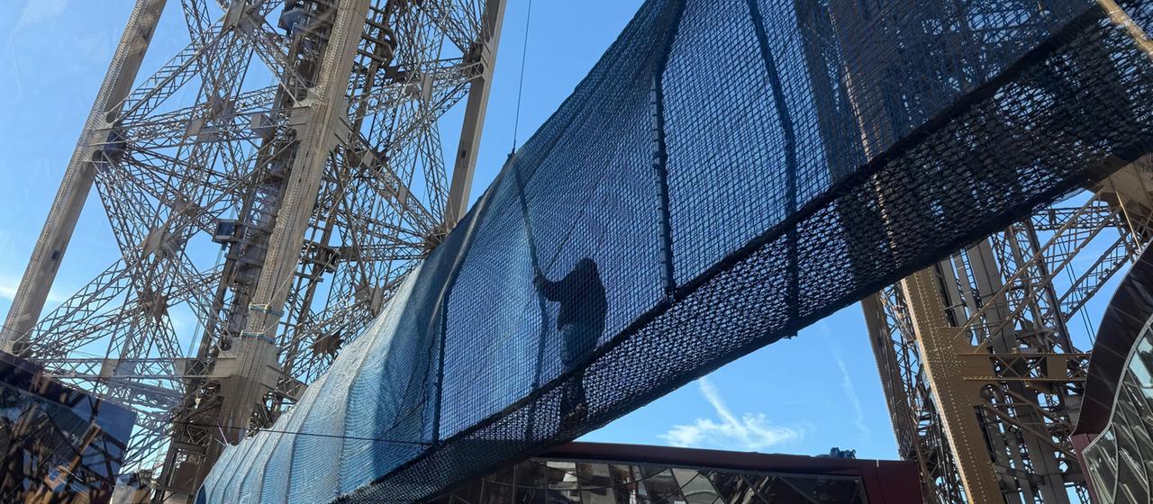 Eine Hängebrücke für Besucher ist zwischen zwei Pfählen des Eiffelturms gespannt.