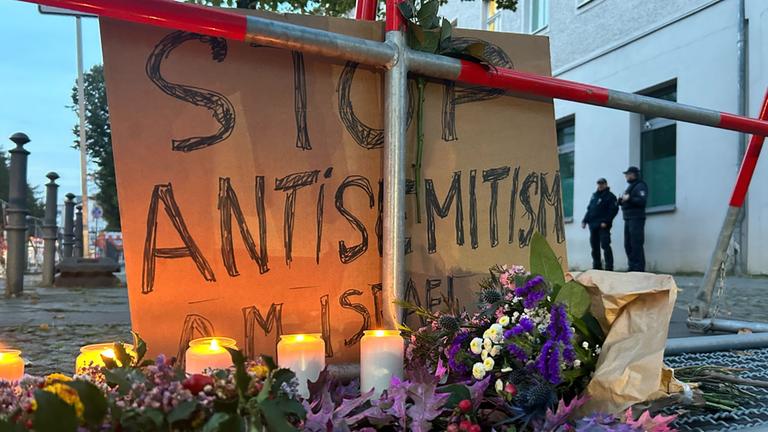 Kerzen stehen vor einem Schild mit der Aufschrift "Stop Antisemitismus".