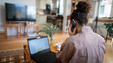 Eine Frau arbeitet im Homeoffice am Laptop und telefoniert (Symbolfoto).