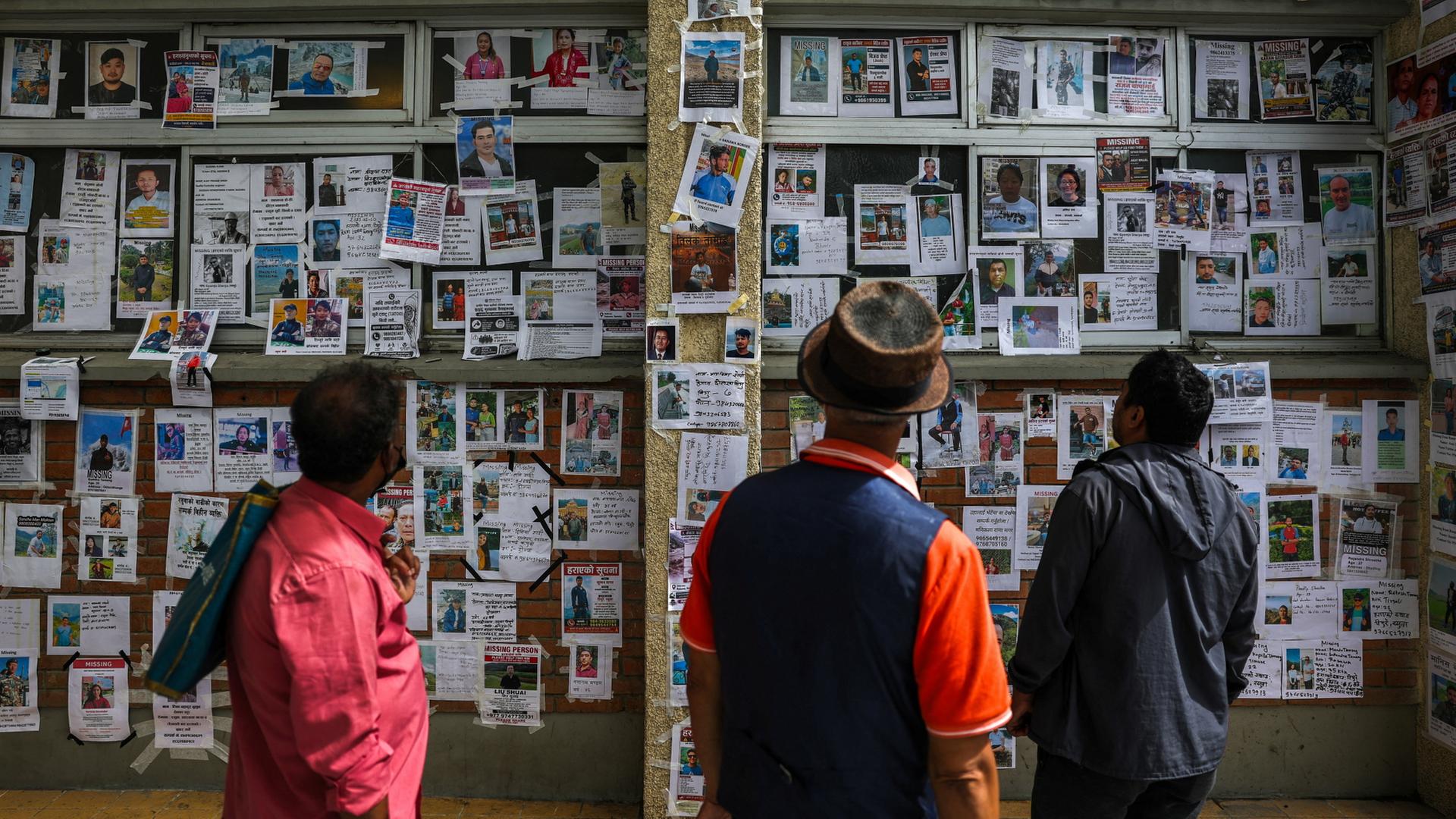 Drei Männer schauen auf eine Wand voller Bilder und Fotos von Vermissten nach der Sturzflut in Nepal. | REUTERS