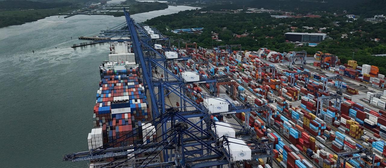 Zahlreiche Container sind an einem Hafen an einer Wasserstraße aufgetürmt