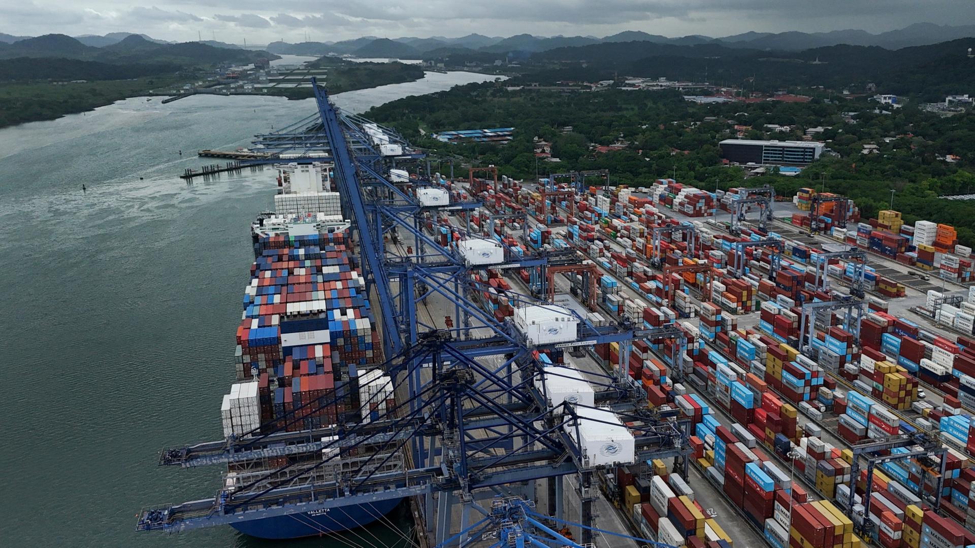 Zahlreiche Container sind an einem Hafen an einer Wasserstraße aufgetürmt | Matias Delacroix/AP/dpa