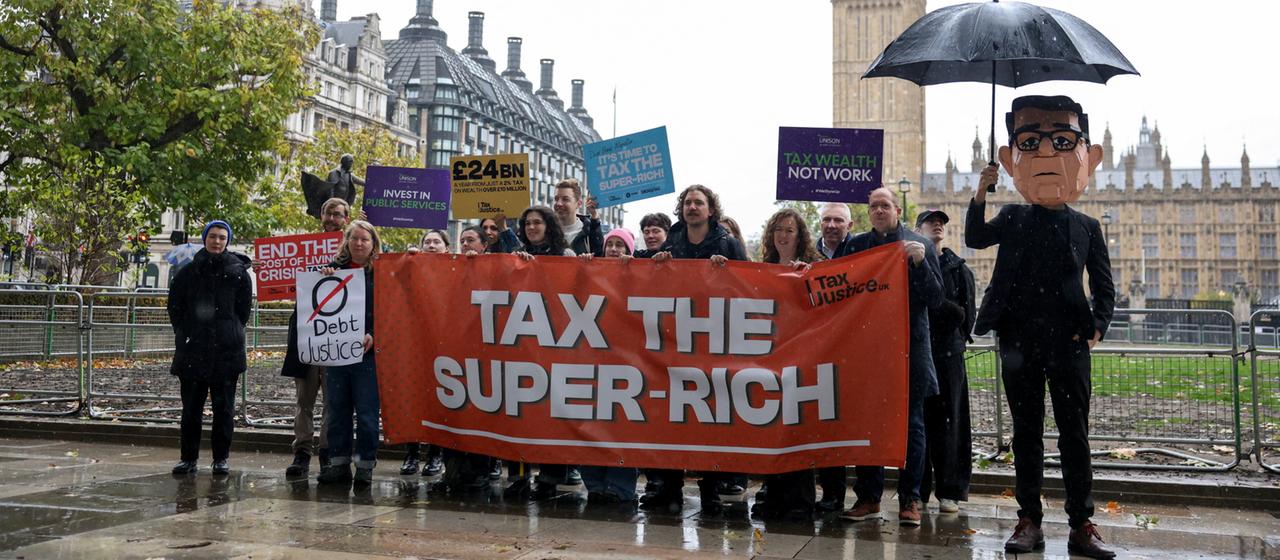 Demonstranten halten während einer Kundgebung in London ein Transparent mit der Aufschrift "Tax the Super Rich" neben einer Puppe des britischen Premierministers Andy Burnham hoch.