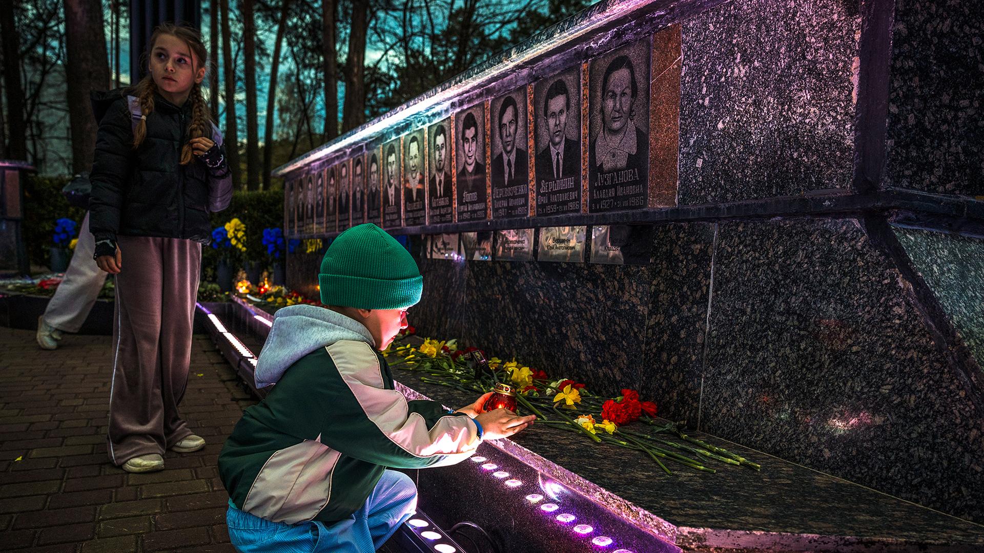 2 Kinder an einem Denkmal vor dem Blumen liegen und Kerzen stehen | EPA