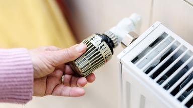 Eine Frau stellt an einem Thermostaten die Temperatur von einem Heizkörper ein.