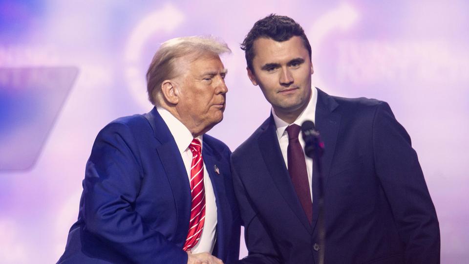 Kirk galt als Unterstützer von US-Präsident Trump - auch im vergangenen Wahlkampf. | picture alliance / ZUMAPRESS.com Donald Trump und Charlie Kirk geben sich auf einer Bühne die Hand. (Archivbild: 22.12.2024)