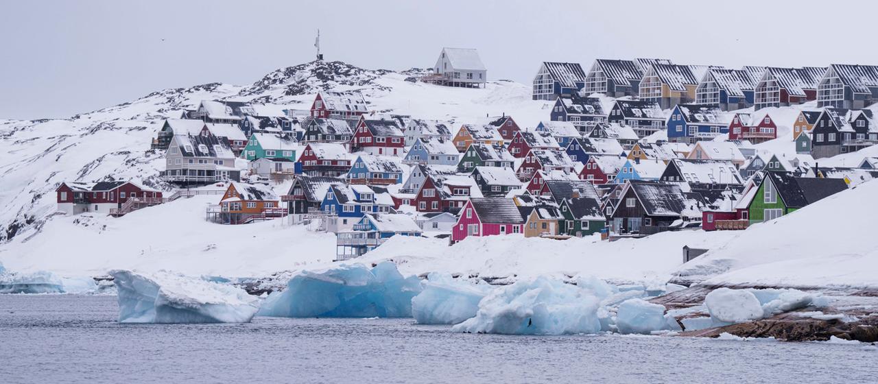 Bunte, schneebedeckte Häuser in Nuuk (Grönland) sind vom Meer aus zu sehen.