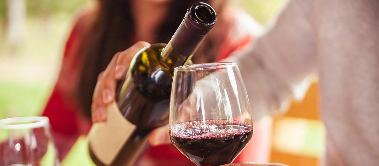 Rotwein wird aus einer Flasche in ein Glas eingeschenkt.