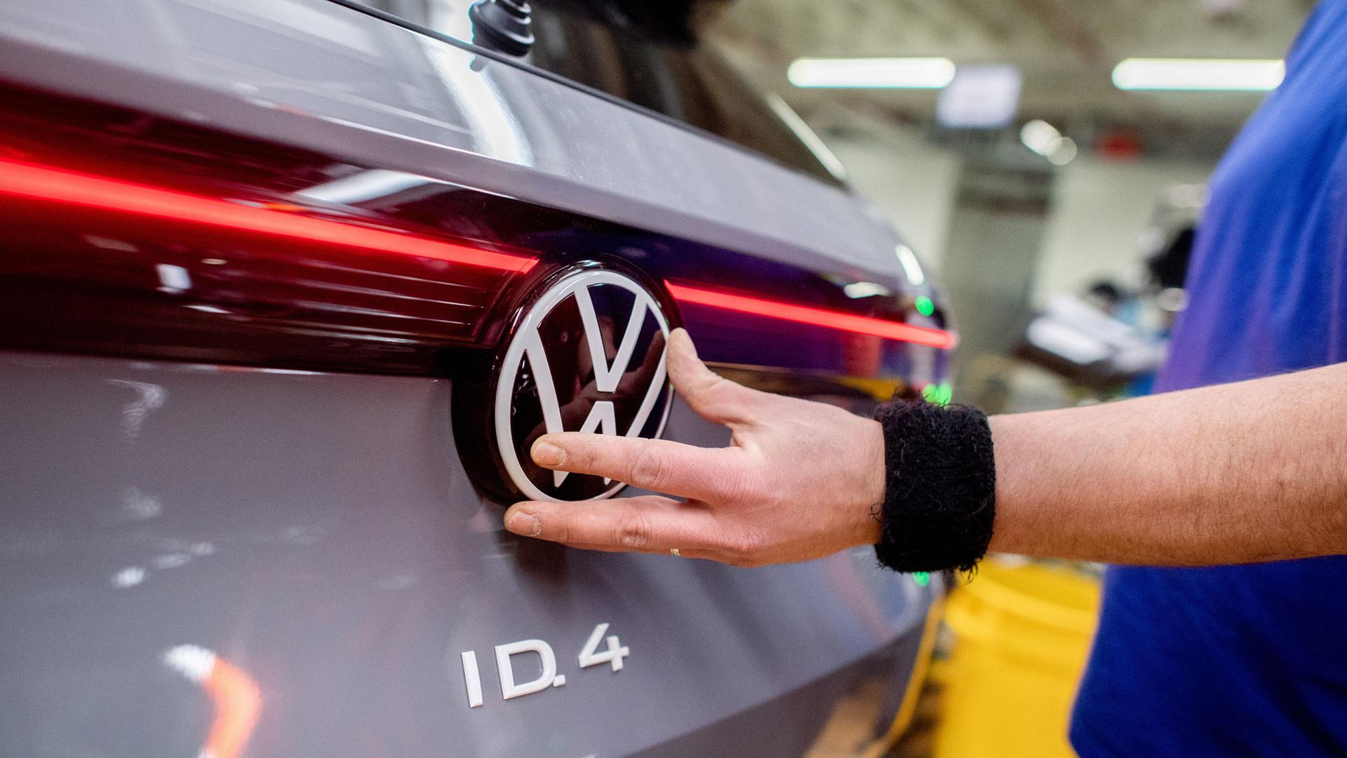 Ein Mitarbeiter setzt im Werk Emden das VW- Logo an einem Fahrzeug ein.  | picture alliance/dpa