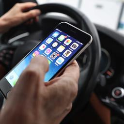 Ein Mann hält ein Handy in der Hand während er Auto fährt (Symbolbild). 