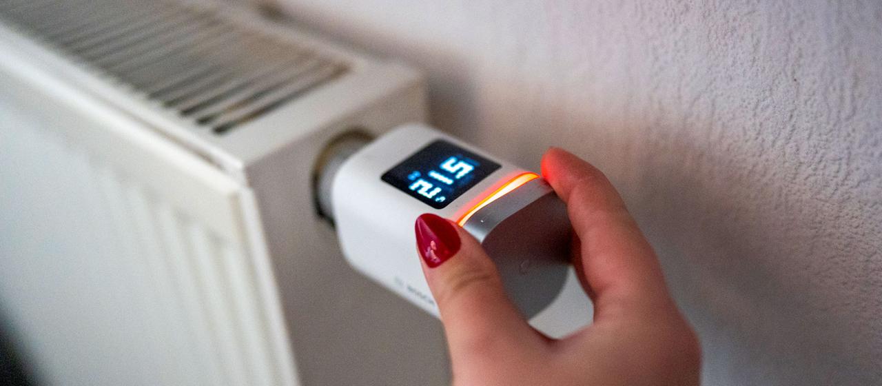 Eine Hand stellt an einem smarten Thermostaten die Temperatur ein.