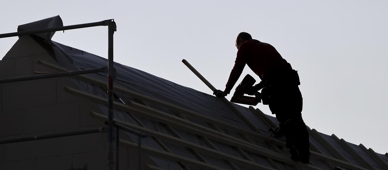 Ein Dachdecker arbeitet an einem Hausdach.