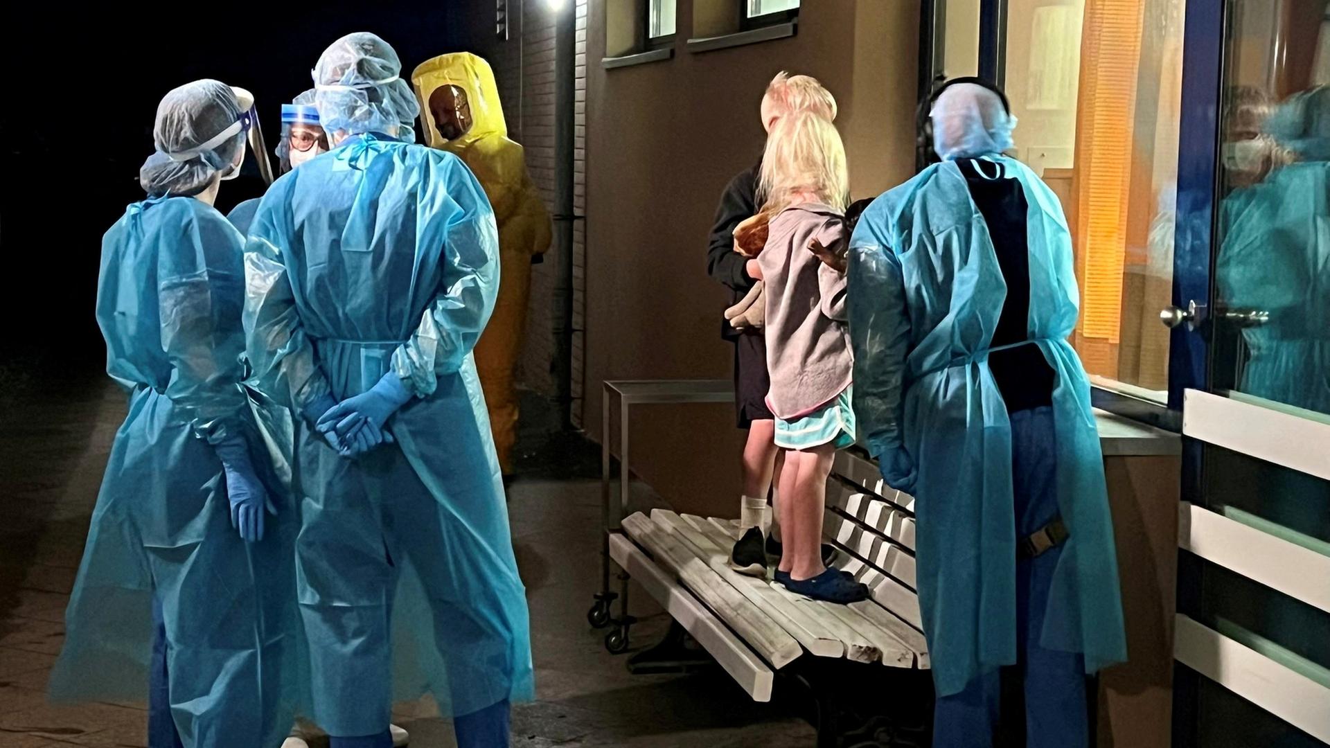 Medizinisches Personal in Schutzkleidung und zwei Kinder schauen durch eine Glasscheibe | via REUTERS