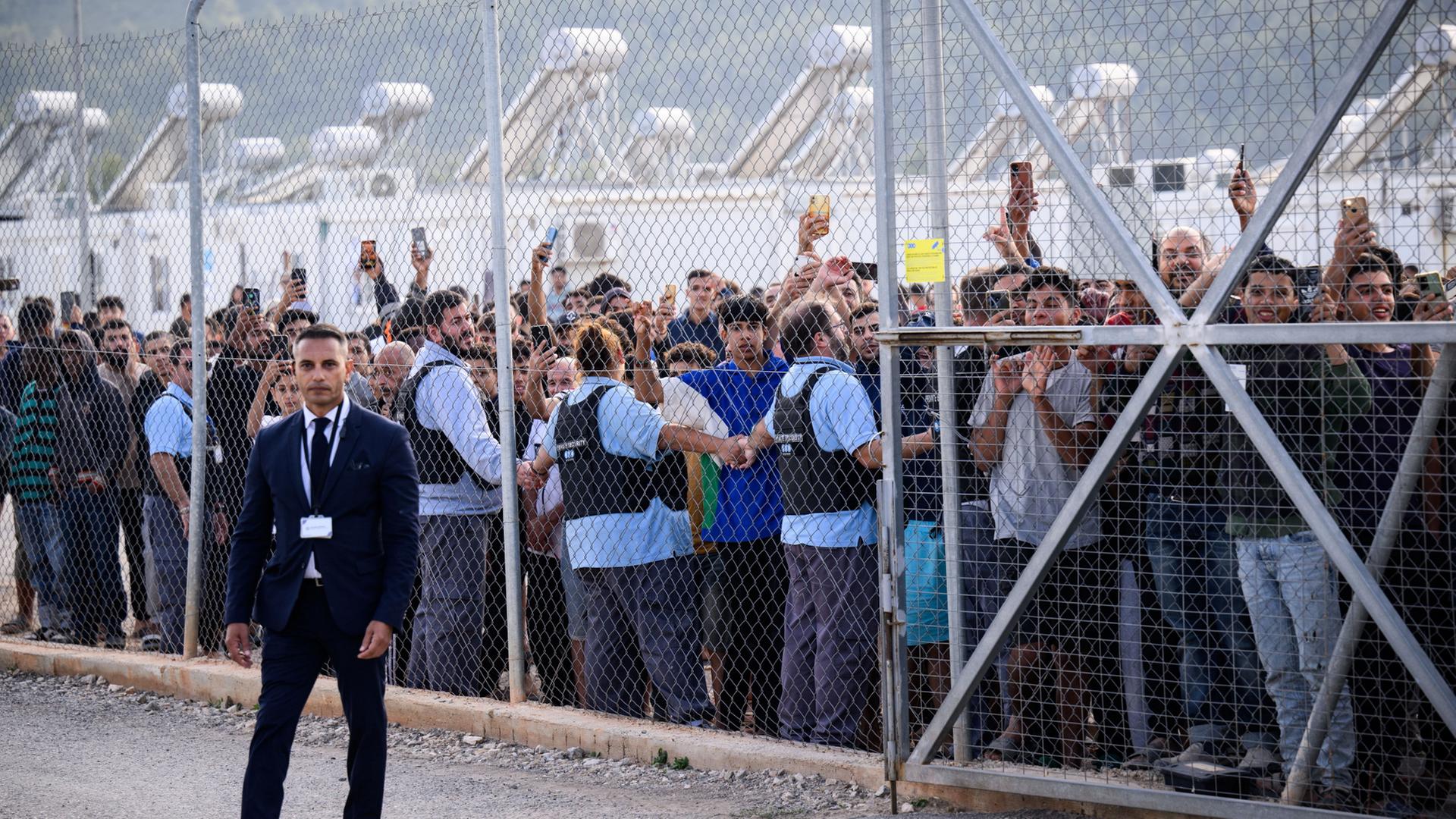 Bewohner des Flüchtlingslagers in Malakasa stehen hinter einem Zaun. | Bernd von Jutrczenka/dpa