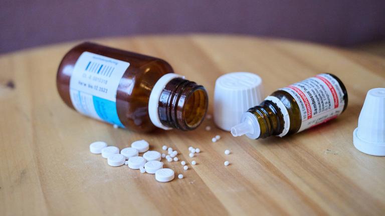 Globuli und homöopathische Tabletten liegen neben Fläschchen auf einem Holztisch