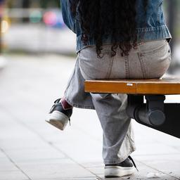 Eine junge Frau sitzt an einer Haltestelle auf einer Bank.