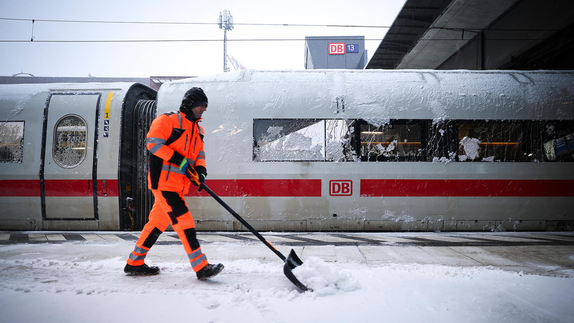 Ein Mitarbeiter schiebt Schnee von einem Bahnsteig am Hamburger Hauptbahnhof, an dem ein abgestellter ICE steht. | dpa