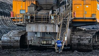 : Ein Mitarbeiter der Lausitz Energie Bergbau AG (LEAG) klettert auf eine riesige Fördermaschine am Kohleflöz im Braunkohletagebau Jänschwalde.
