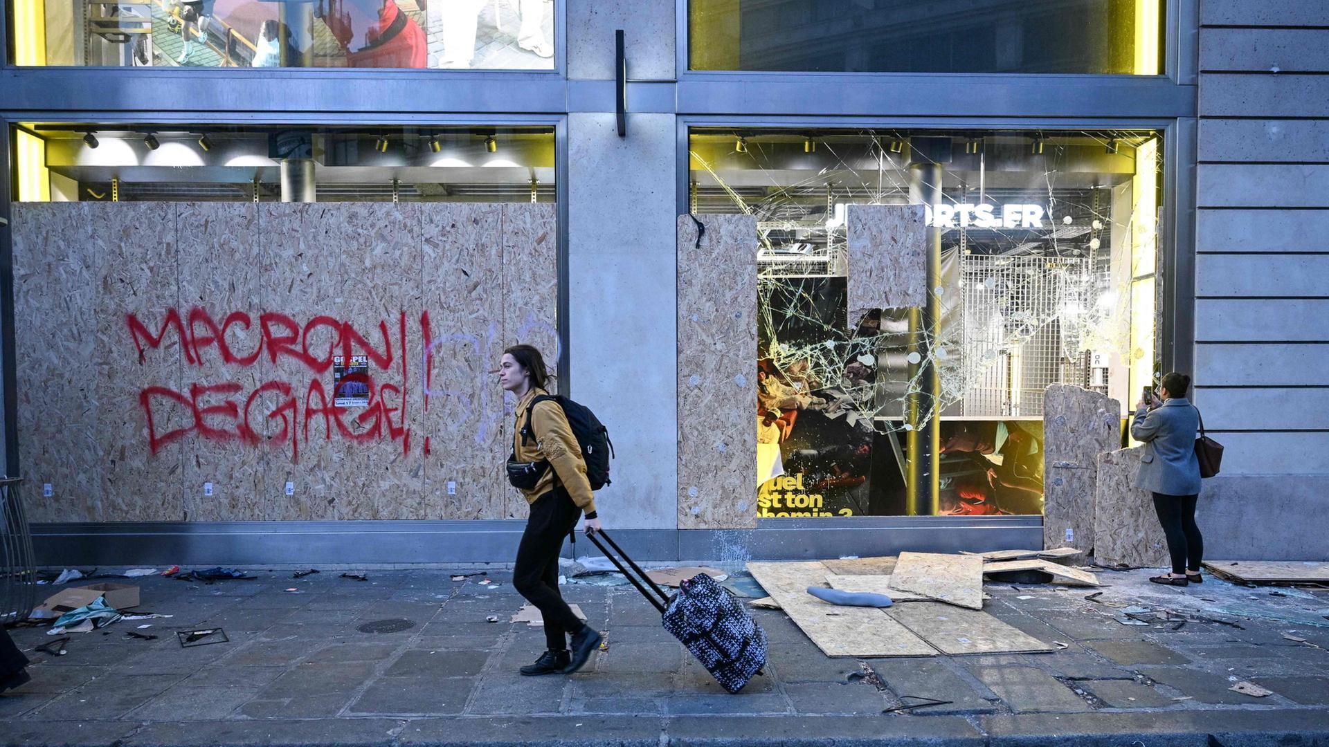 Eine Fußgängerin geht an einem beschädigten Geschäft in Paris vorbei. | Matthieu Rondel/AFP/dpa