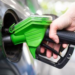 Eine Frau hält an einer Tankstelle an einer Zapfsäule eine Zapfpistole in der Hand und betankt ein Auto.