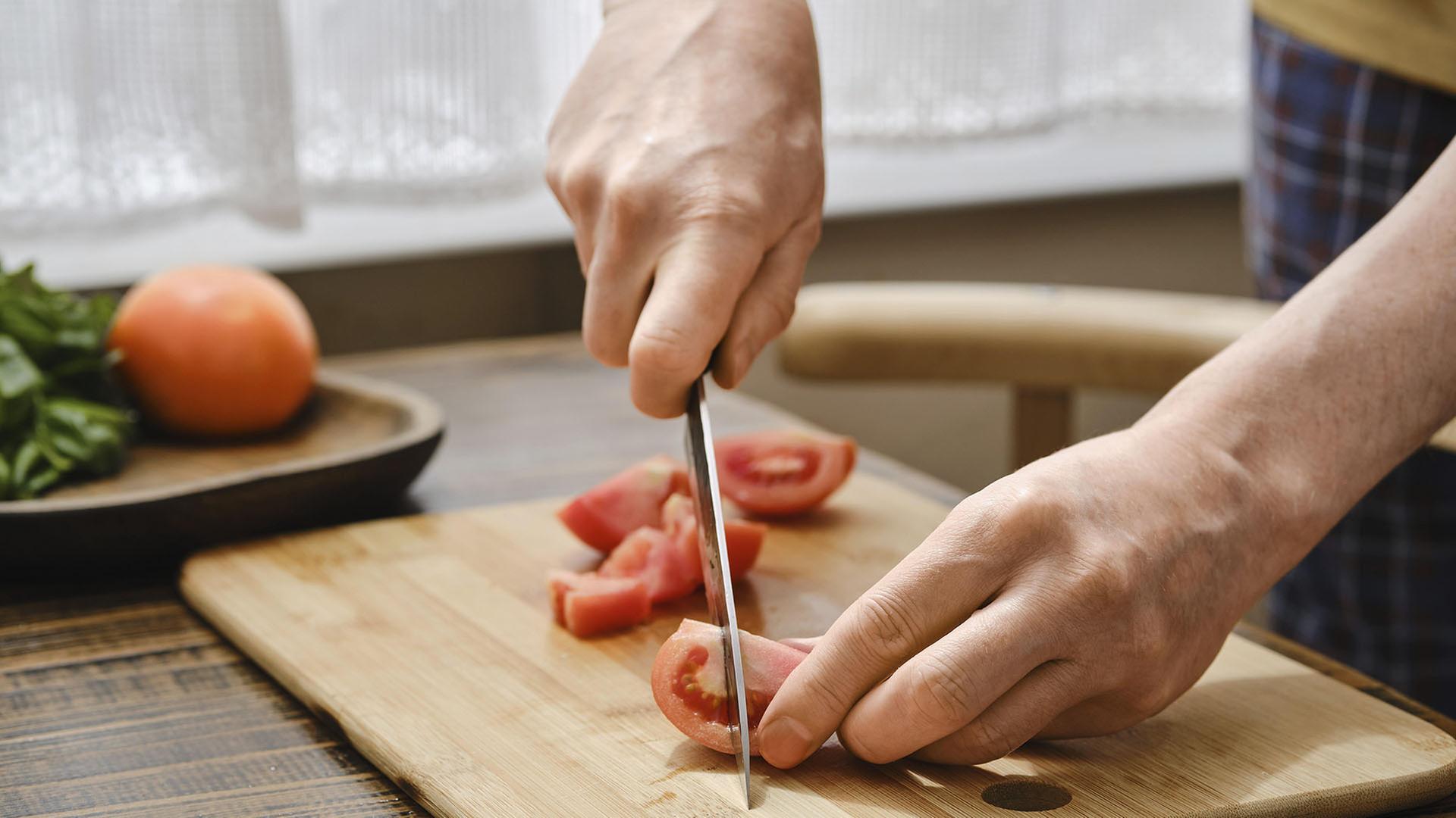 Eine Person schneidet eine Tomate auf einem Holzbrett. | picture alliance / imageBROKER