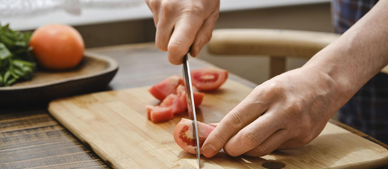 Eine Person schneidet eine Tomate auf einem Holzbrett.
