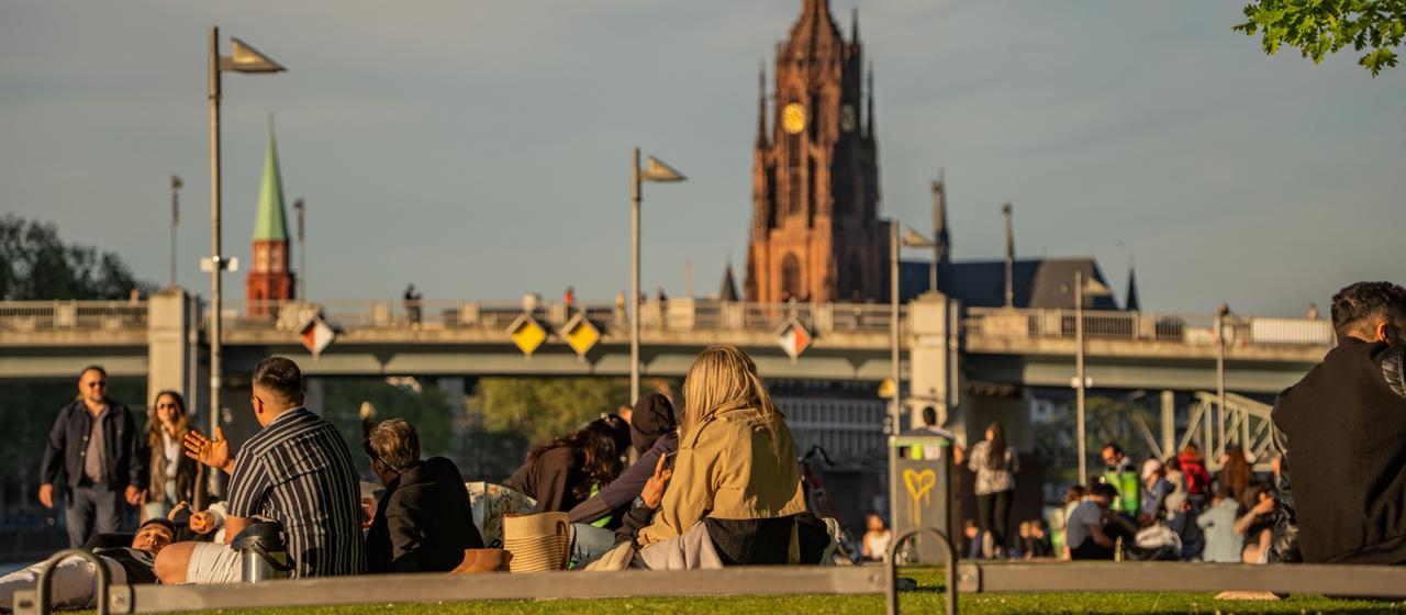 Menschen sitzen in den Abendstunden bei angenehmen Temperaturen am Mainufer.
