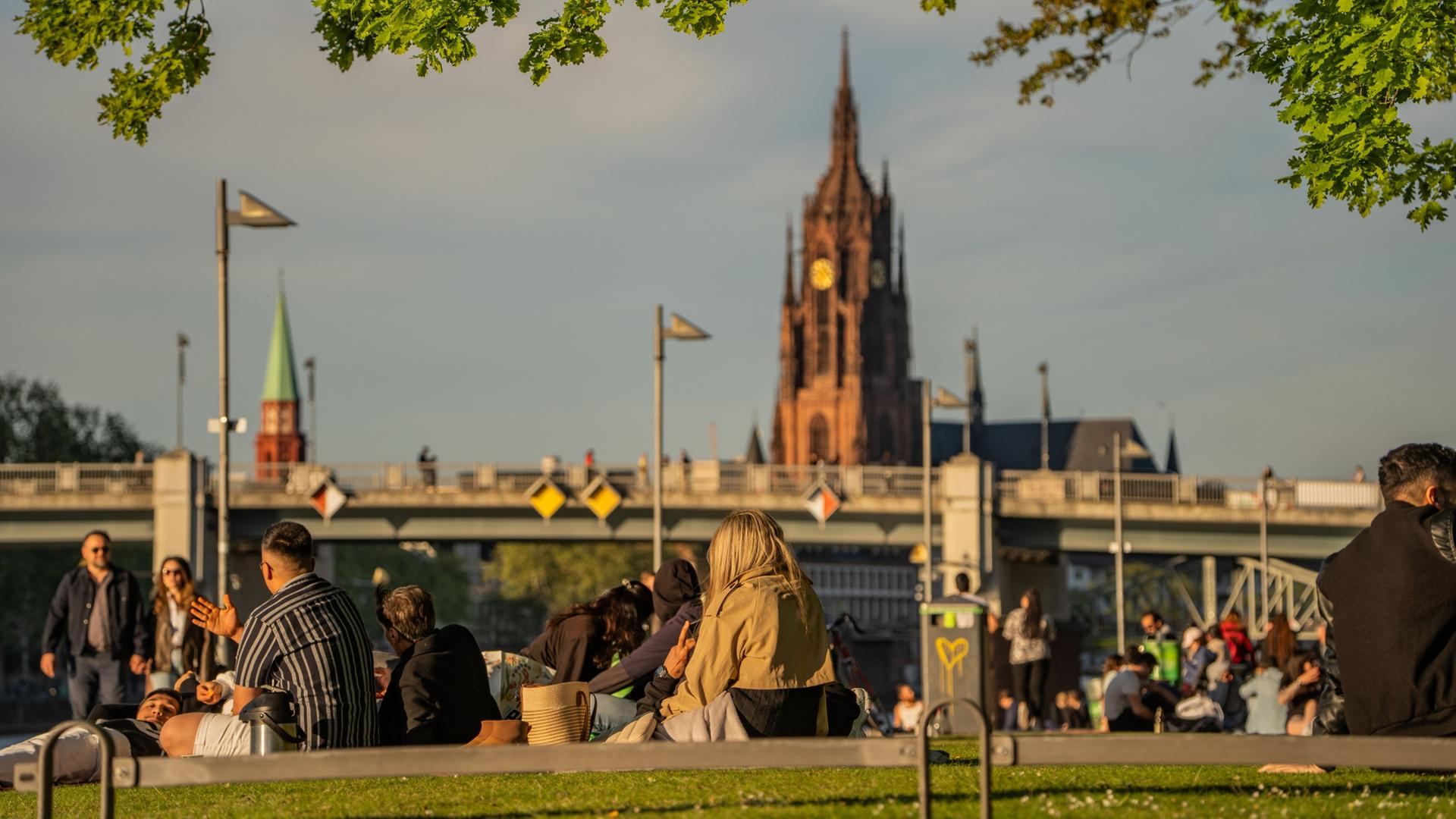 Menschen sitzen in den Abendstunden bei angenehmen Temperaturen am Mainufer. | Andreas Arnold/dpa