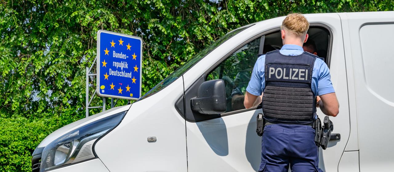 Polizist steht vor einem weißen Lieferwagen an der deutschen Grenze