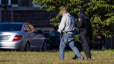 Ein Mann wird von einem Bundespolizisten zu einem Auto geführt.