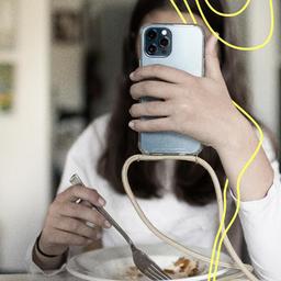 Ein junges Mädchen schaut auf ihren Handybildschirm während sie etwas isst.