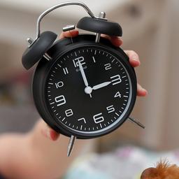 Eine aufwachende Frau hält einen Wecker.