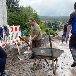 Menschen räumen nach Überflutung Schlamm von einer Straße.